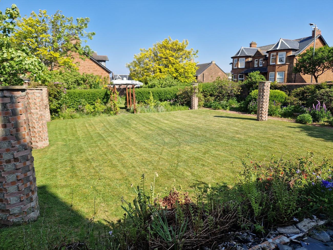 A large striped lawn with borders and a pergola.
